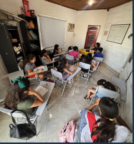 Alumnos en clase presencial de inglés, sentados frente a la docente al fondo del aula.